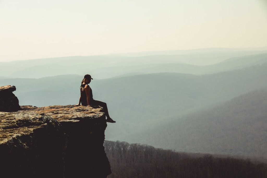 Woman sitting on edge of a cliff with mountain vista in distance